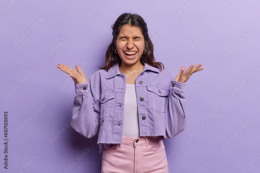 Ecstatic woman overflows with joy exclaimes exuberantly bursts from happiness spreads happiness to everyone around her dressed in stylish cropped jacket and trousers isolated over purple background Ecstatic woman overflows with joy exclaimes exuberantly bursts from happiness spreads happiness to everyone around her dressed in stylish cropped jacket and trousers isolated over purple background