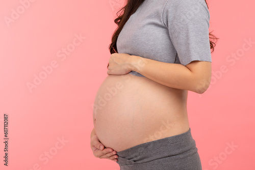 Side view Close up Pregnant Woman standing stroking big belly with love isolated on pink background. Pregnancy of young woman enjoy with future life. Motherhood and Pregnant Concept
