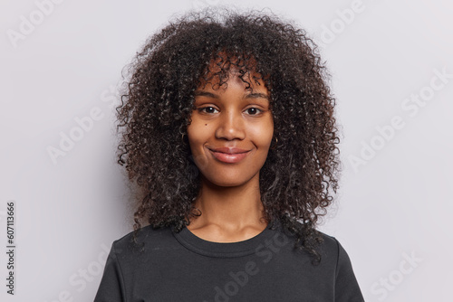 Tableau sur toile Portrait of pleased teenage girl with curly frizzy hair smiles gently expresses