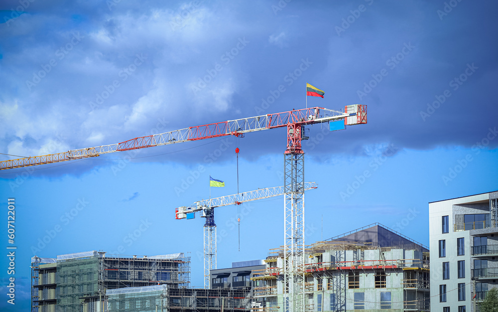 Construction site with cranes with flags Lithuanian and Ukrainian building residential buildings on blue sky background with fluffy dark clouds