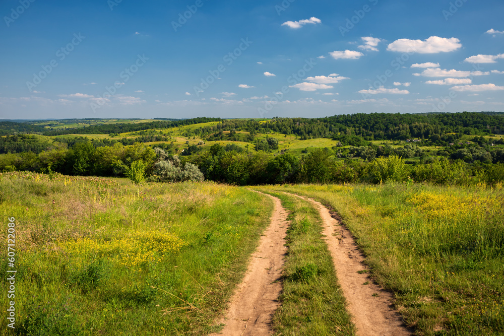 summer country road amidst green hills and blue sky with white clouds