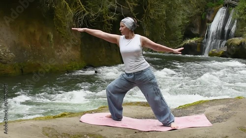 Active Woman Practicing Yoga by the river in front of a beautiful waterfall photo