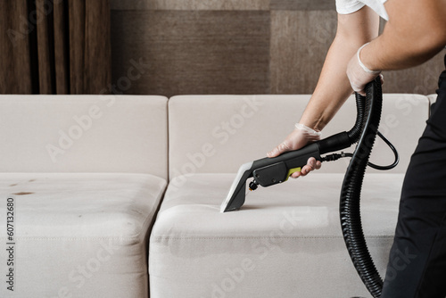 Fotografie Housekeeper is extracting dirt from upholstered sofa using dry cleaning extractor machine