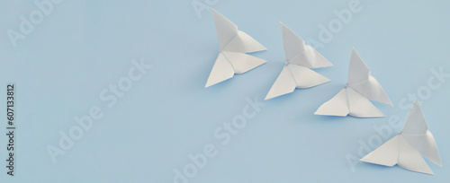 Fototapeta Naklejka Na Ścianę i Meble -  White paper origami butterfly on blue background. World Day of Peace. Day Against Humiliation. International Day Of Human Fraternity. International Day of Living Together in Peace. Banner