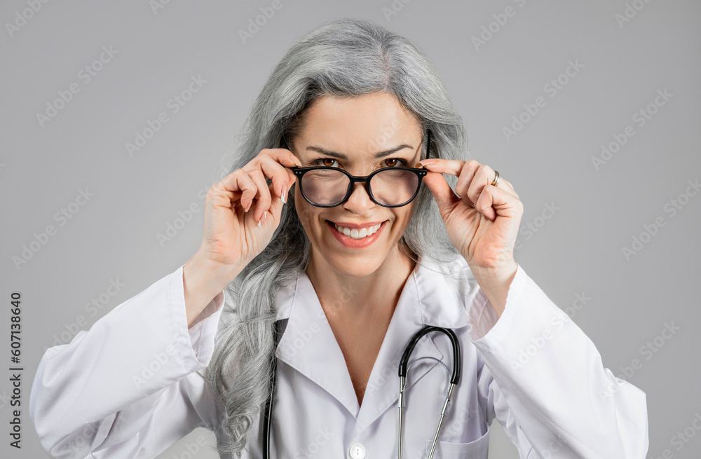 Woman Doctor Looking At Camera Through Eyeglasses Over Gray Background