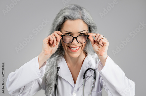 Woman Doctor Looking At Camera Through Eyeglasses Over Gray Background