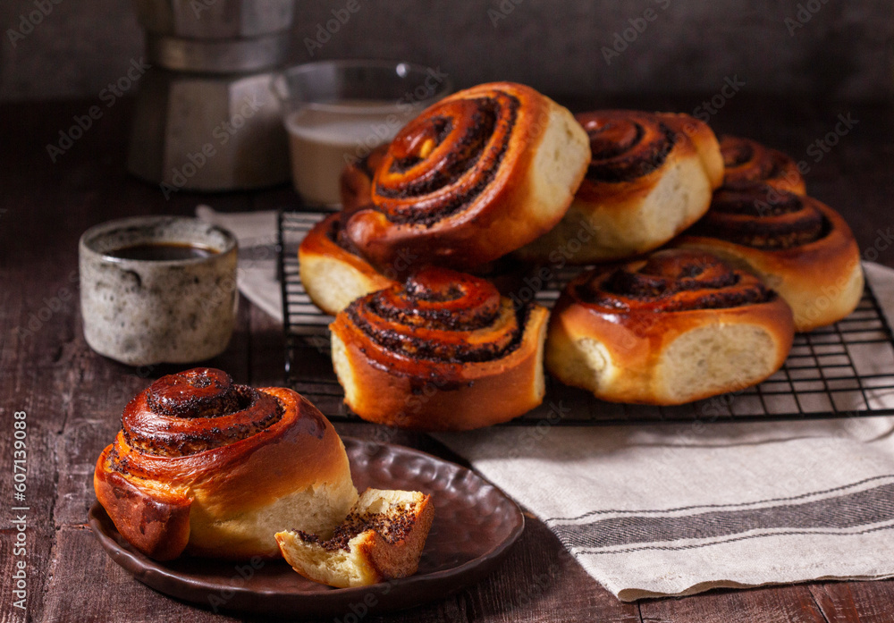 Yeast dough cinnabons with poppy seeds, raisins and candied fruits, served with coffee. Rustic style.