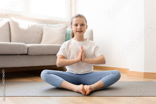 Smiling caucasian middle aged girl in sportswear practicing yoga, meditates on mat in living room