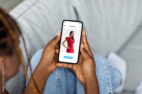 Young black woman shopping online at phone, look at new clothes at screen at home, enjoy mobile app