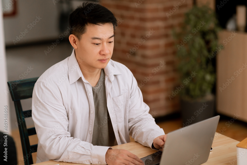 Focused middle aged asian man using laptop, working online from home, having online business meeting, copy space Focused middle aged asian man using laptop, working online from home, having online business meeting, copy space