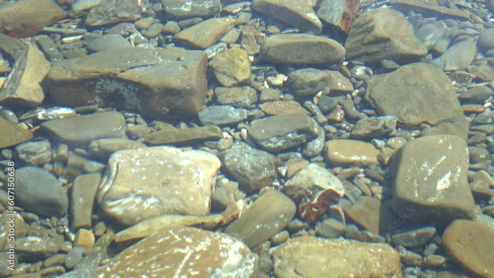 Small waves on the Adriatic Sea, stones and a pebbly bottom, illuminated by the rays of the sun, view from above, background Small waves on the Adriatic Sea, stones and a pebbly bottom, illuminated by the rays of the sun, view from above, background
