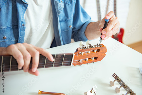 Guitar Master hands placing and adjusting with a screwdriver the peg of a classical instrument. Unrecognizable person