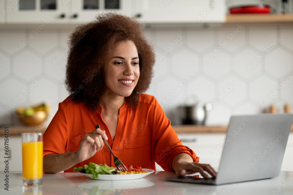 Smiling Young Black Female Using Laptop Computer During Breakfast In Kitchen Smiling Young Black Female Using Laptop Computer During Breakfast In Kitchen