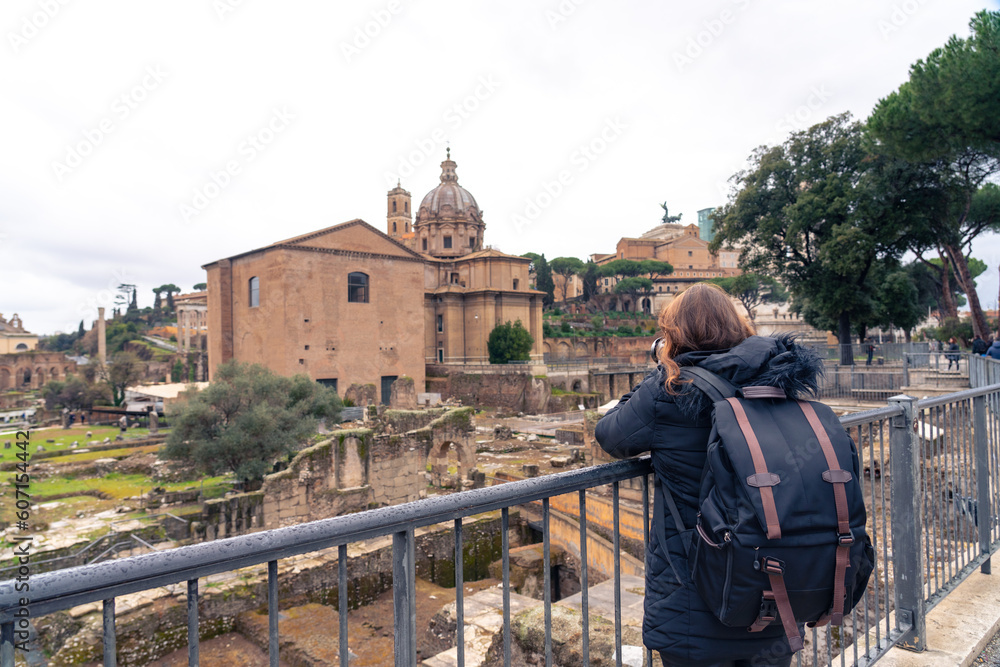 Unrecognizable full body Latin woman traveler tourist with backpack admiring on paved square and enjoying amazing and majestic cityscape with Roman Forum in Rome, Italy during vacation
