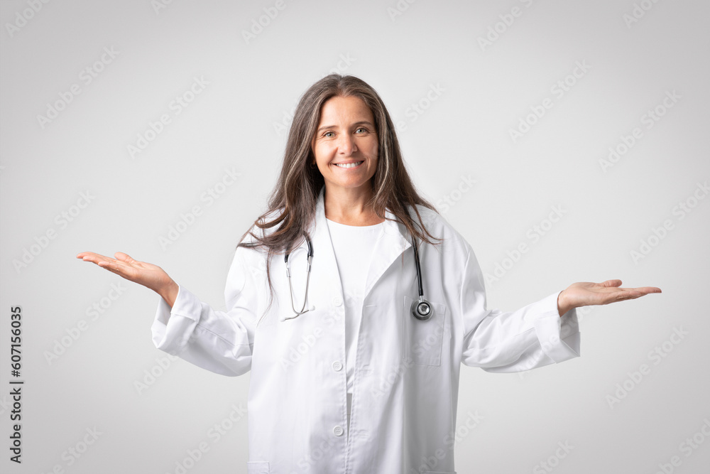 Cheerful european woman doctor holding something invisible on both hands palms smiling at camera, grey background Cheerful european woman doctor holding something invisible on both hands palms smiling at camera, grey background