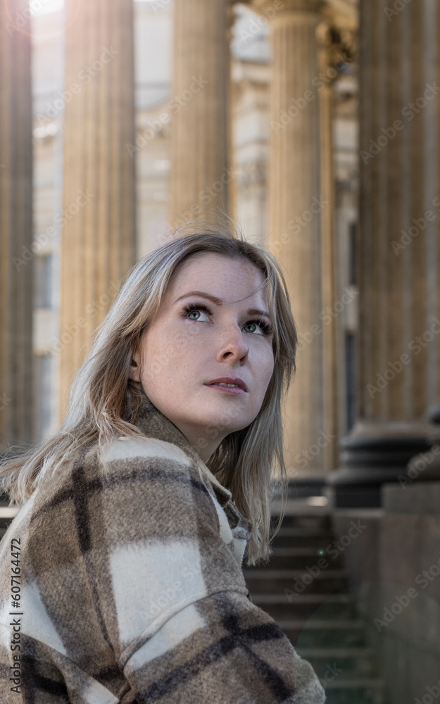 portrait of a young blonde girl against the backdrop of columns. backlight, a beautiful relief from the shade, a spring walk on the street on a sunny day. human close up
