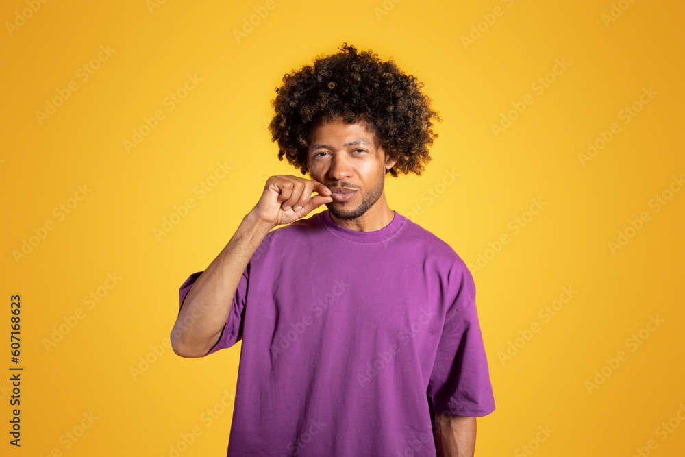 Glad mature black curly guy in violet t-shirt making closed mouth gesture, keeping a secret Glad mature black curly guy in violet t-shirt making closed mouth gesture, keeping a secret
