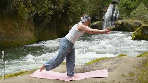 Woman is practicing yoga on beach by the river in front of a beautiful waterfall photo