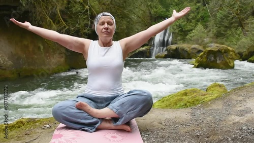 50+ old woman is practicing yoga by the river in front of a beautiful waterfall photo