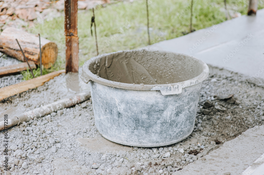 A bowl, a bucket, a concrete mixer in concrete, cement stands on stones at a construction site.