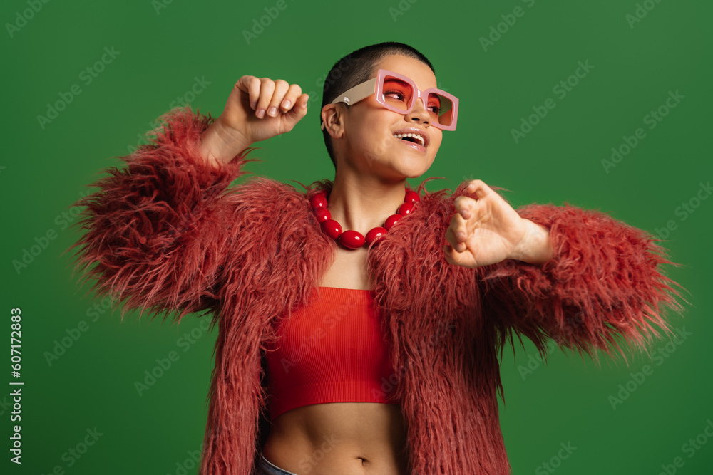Excited young short hair woman in trendy clothes dancing against green background - obrazy, fototapety, plakaty 