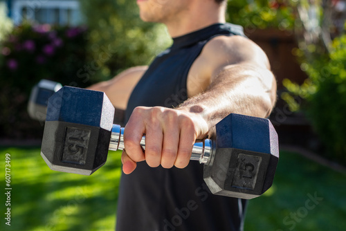 Young adult male doing lateral raises to target his shoulders during an afternoon at-home workout on a yoga mat during the coronavirus pandemic.