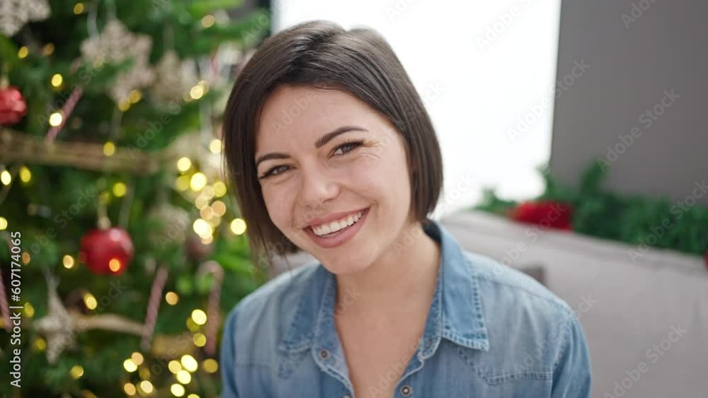 Young caucasian woman smiling sitting by christmas tree at home