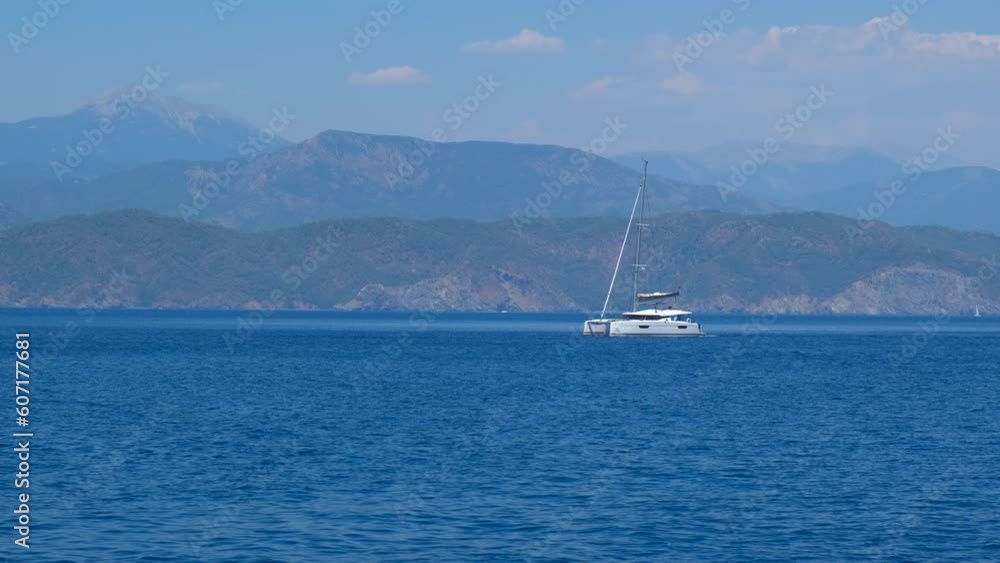 Catamaran anchored in azure sea. A nice white anchored catamaran against tropical coast in the day light. A concept of sailing hobby in the open air water. Catamaran anchored in azure sea. A nice white anchored catamaran against tropical coast in the day light. A concept of sailing hobby in the open air water.