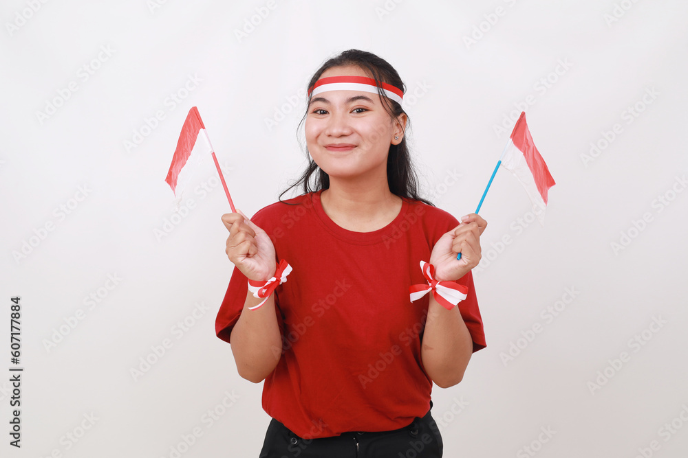 Fototapeta premium Cheerful young indonesian girl standing while holding red white flag. Isolated on white