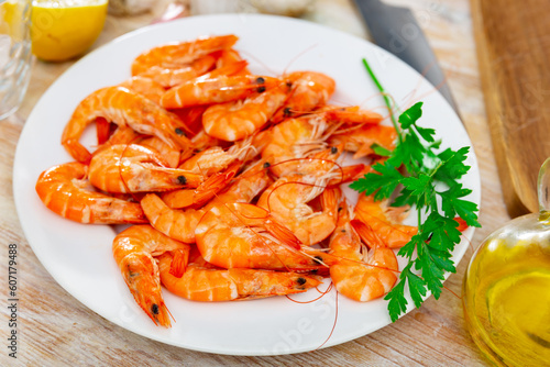 Whole raw red shrimps with lemon, cloves of garlic, fresh greens and olive oil on plate. Popular seafood delicacies..