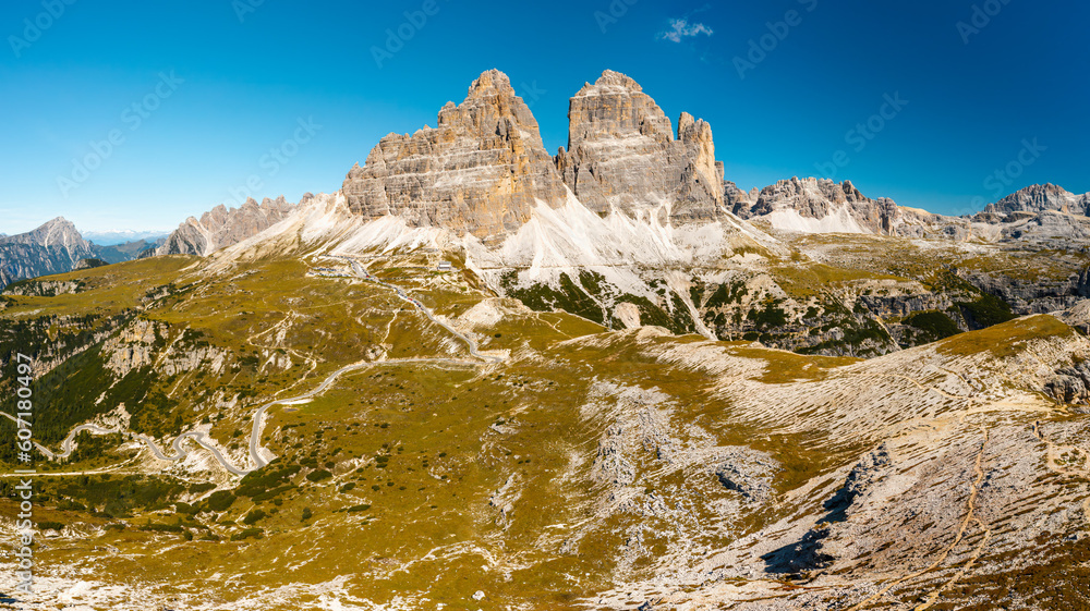 Mountainous terrain at sunrise. Majestic Three Peaks of Lavaredo with sand-covered foothills in Alps at beginning of sunny day aerial view in back lit