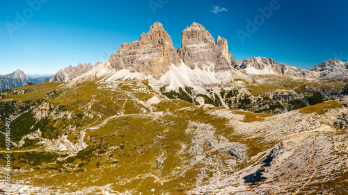 Mountainous terrain at sunrise. Majestic Three Peaks of Lavaredo with sand-covered foothills in Alps at beginning of sunny day aerial view in back lit