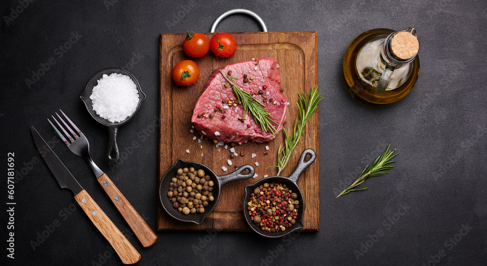 Raw piece of beef with spices pepper, rosemary sprig, salt and olive oil on a wooden board, black background Raw piece of beef with spices pepper, rosemary sprig, salt and olive oil on a wooden board, black background
