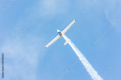 Top view of a gliders plane flying and doing tricks and stunts over the blue sky with white steam wake on a summer day at Gijon air show festival