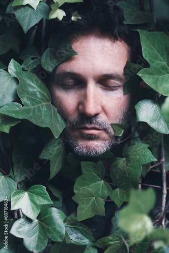 Face of a man with closed eyes in the middle of ivy leaves