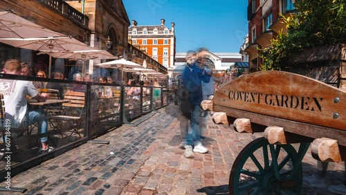 Covent Garden area name sign on a wooden cart with flowers on a street in Covent Garden, London, UK during a bright summer day. People rushing through a district in London. photo