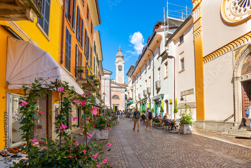 The Church of Saint Stefano or Parrocchia Santo Stefano in the distance from a cobblestone alley of shops and sidewalk cafes in Menaggio  Italy  on Lake Como.