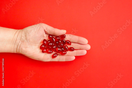 Fotografie Krill oil capsules in a womans hand on a red background