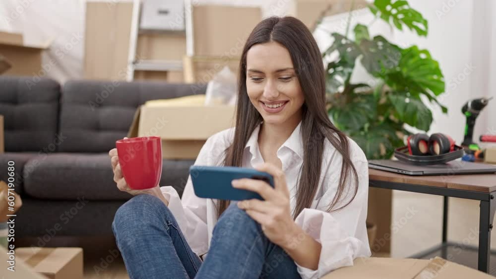 Young beautiful hispanic woman using smartphone drinking coffee sitting on floor at new home Young beautiful hispanic woman using smartphone drinking coffee sitting on floor at new home