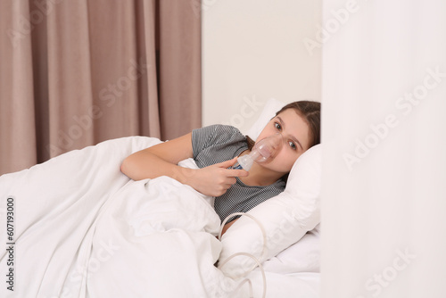 Cute girl using nebulizer for inhalation on bed at home