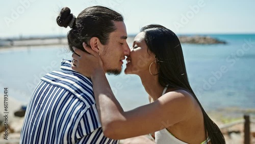 Man and woman couple smiling confident sitting on bench kissing at seaside