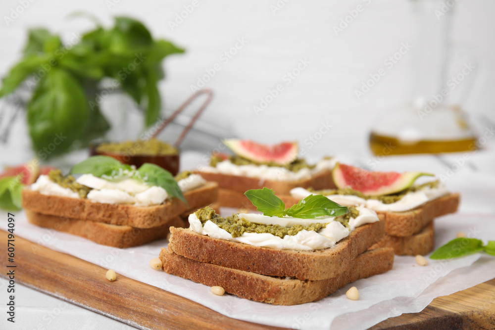 Tasty bruschetta with cream cheese, pesto sauce and fresh basil on parchment paper, closeup