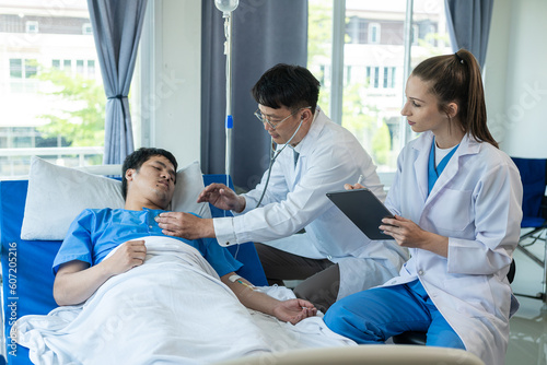 Photography A female doctor and two male doctors treat a young male patient in bed and are talking to an Asian male patient beside the hospital bed in a hospital emergency room