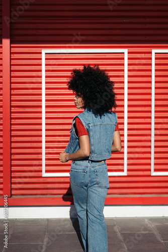 Woman in blue denim vest standing near red roll up door
