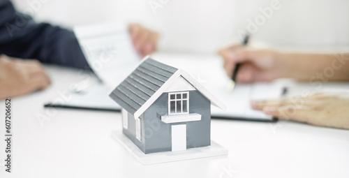 A real estate agent with a home model is talking to clients about renting a house and buying home insurance and contracting the contract after the formal negotiation is completed