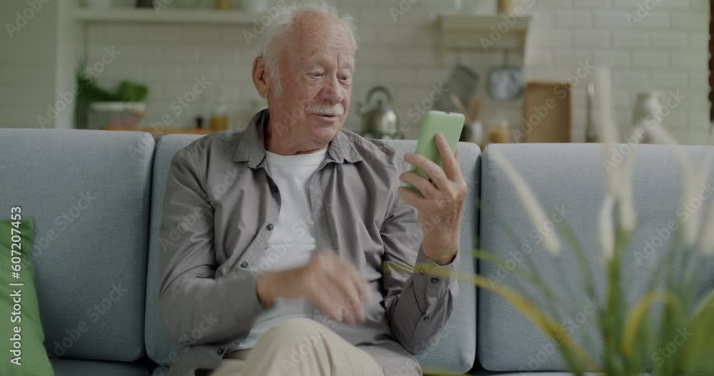 Senior man making online video call talking using smartphone indoors in living room at home. Communication and modern technology concept. Senior man making online video call talking using smartphone indoors in living room at home. Communication and modern technology concept.