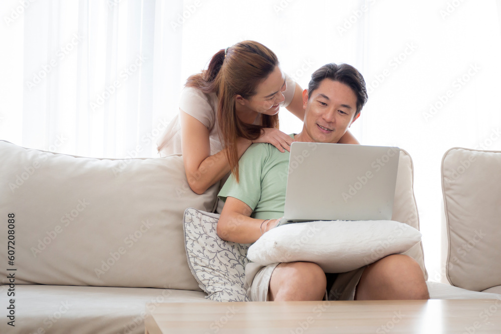 Young asian couple using laptop computer for looking social media or video with relax and leisure on sofa in the living room at home, man and woman watching laptop to internet, lifestyles concept. Young asian couple using laptop computer for looking social media or video with relax and leisure on sofa in the living room at home, man and woman watching laptop to internet, lifestyles concept.