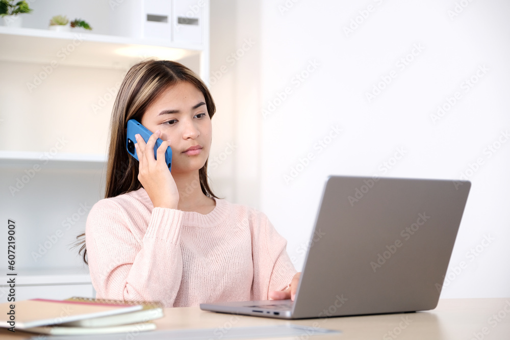Young asian woman talking mobile phone while working with laptop computer, work at home, online learning Young asian woman talking mobile phone while working with laptop computer, work at home, online learning