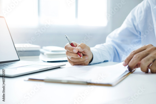 Asian businessman reviewing document reports at office workplace with computer laptop. legal expert, professional lawyer reading and checking financial documents or insurance contract