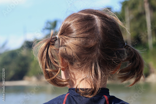 Menina de costas para a foto com o cabelo penteado com duas colas olhando em direção ao rio. photo